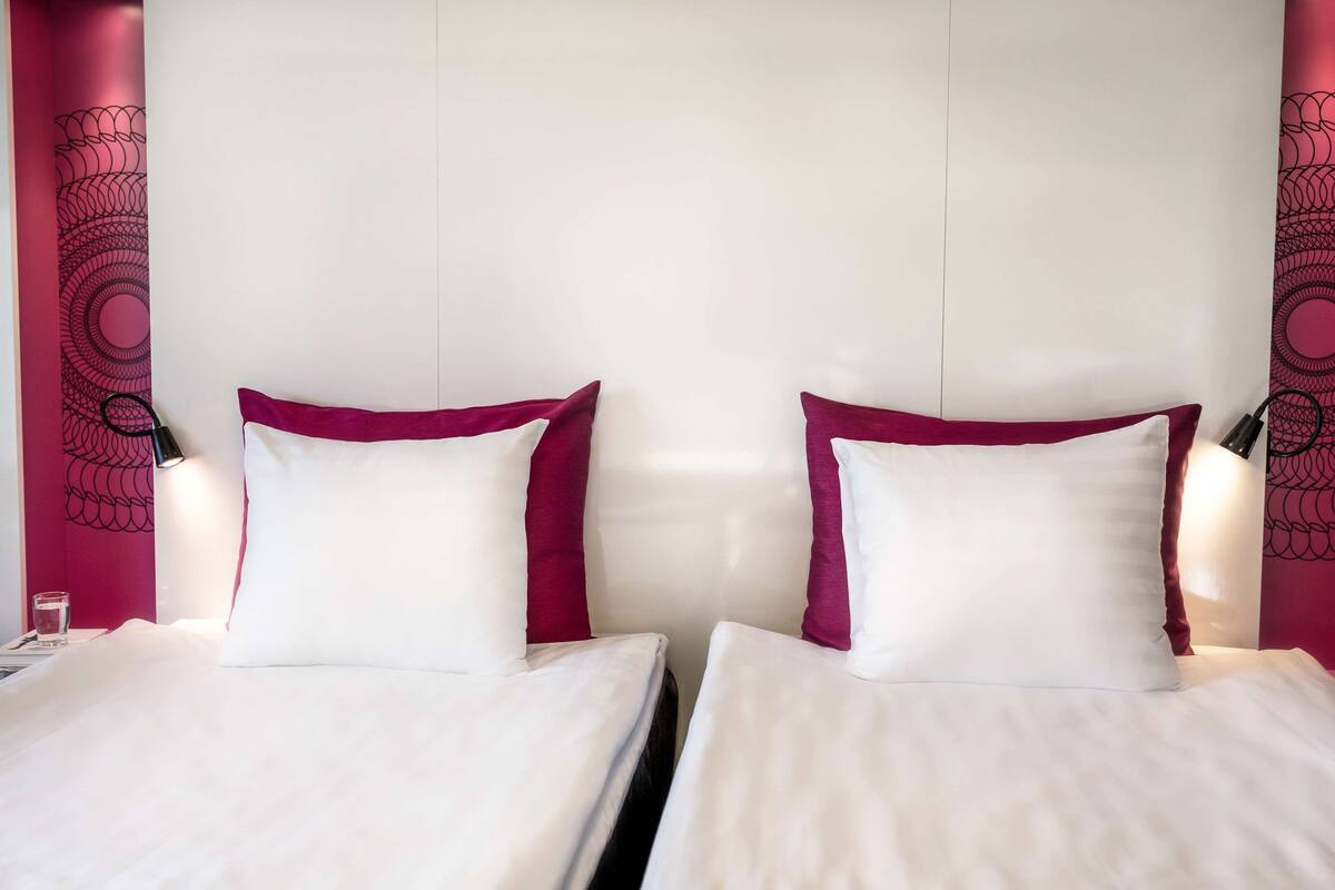 A hotel room with two beds, each with white bedding and maroon pillows.