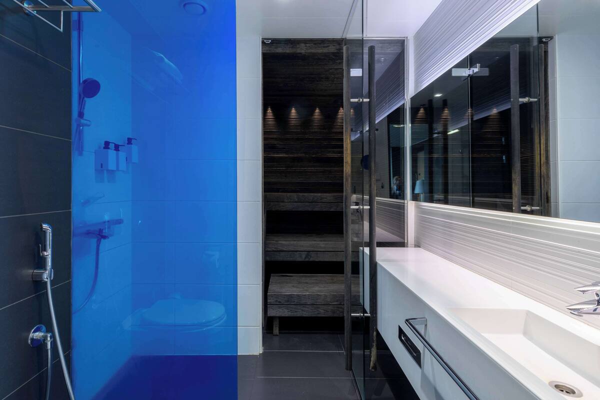 A modern bathroom with a glass shower enclosure, a white sink, and a wooden staircase.