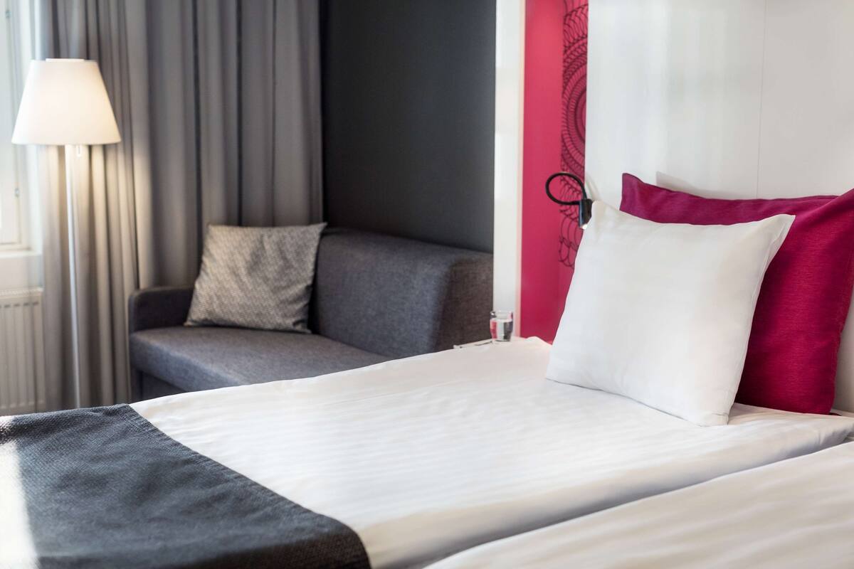 A hotel room with a bed, a sofa, a lamp, and a window with curtains.