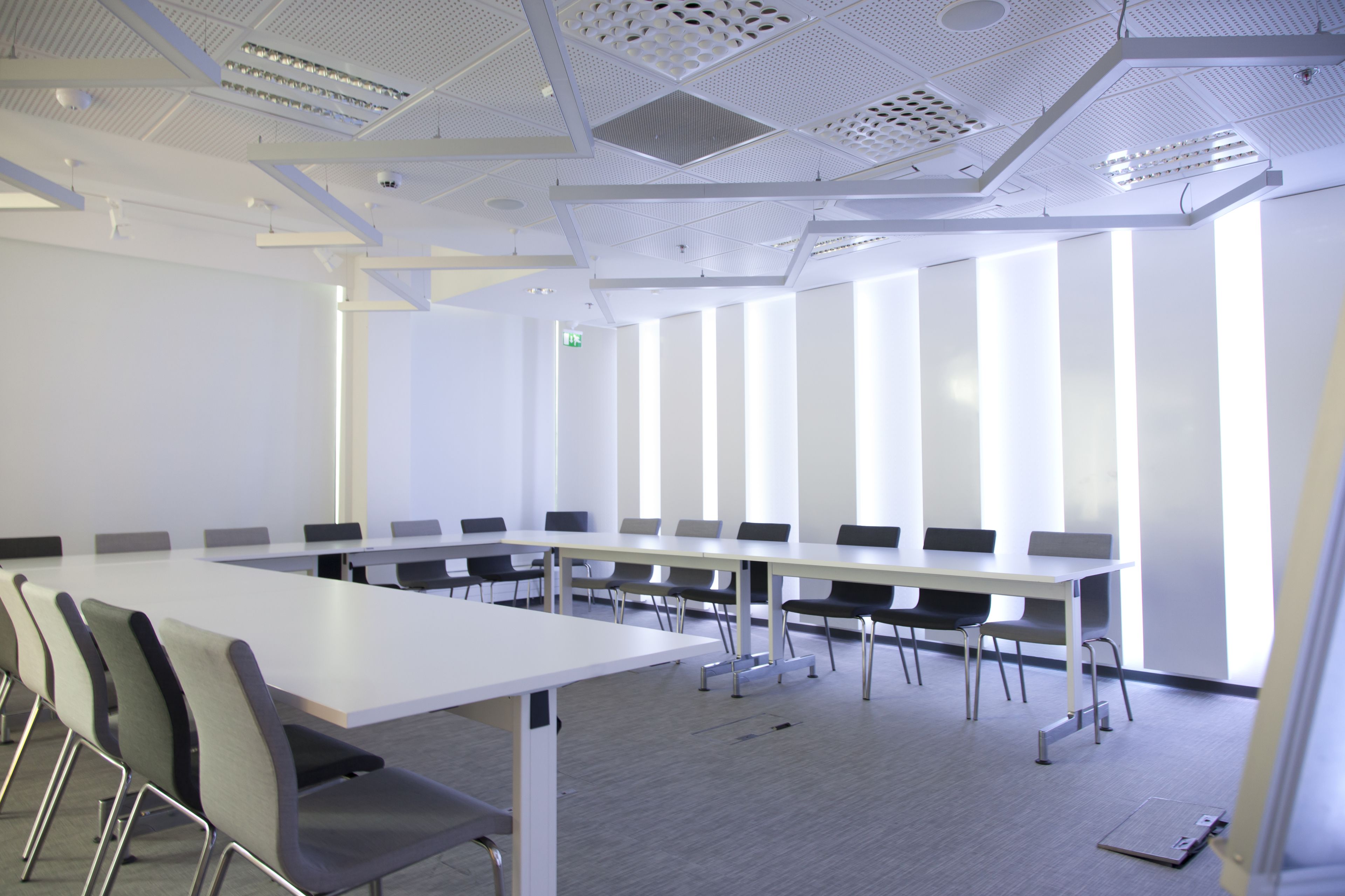 Une salle de conférence dotée d’une longue table, de nombreuses chaises et d’un plafond haut orné de panneaux perforés.