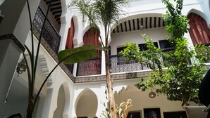 Un patio con arcos, plantas en macetas y un balcón con barandilla decorativa.
