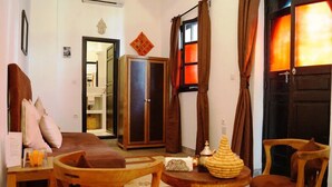 Una habitación tradicional con un sofá de madera, una mesita redonda con un cuenco decorativo, un armario y una puerta con cortinas.