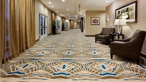 Un couloir d’hôtel avec un tapis à motifs, un coin salon avec des fauteuils et un tableau encadré au mur.