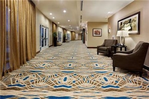 A hotel hallway with patterned carpet, a seating area with chairs, and a framed picture on the wall. - Holiday Inn & Suites San Antonio Northwest by IHG (San Antonio)