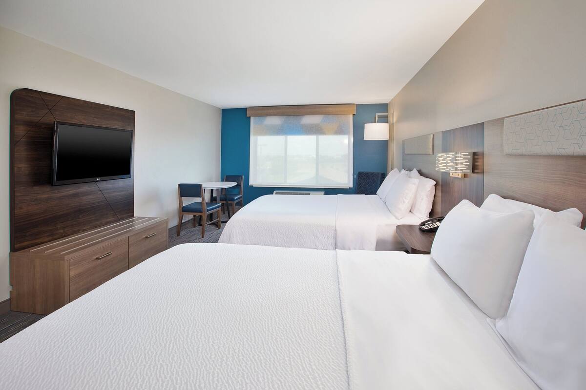 A hotel room with two beds, a flat-screen TV, a desk, and a window with a view.