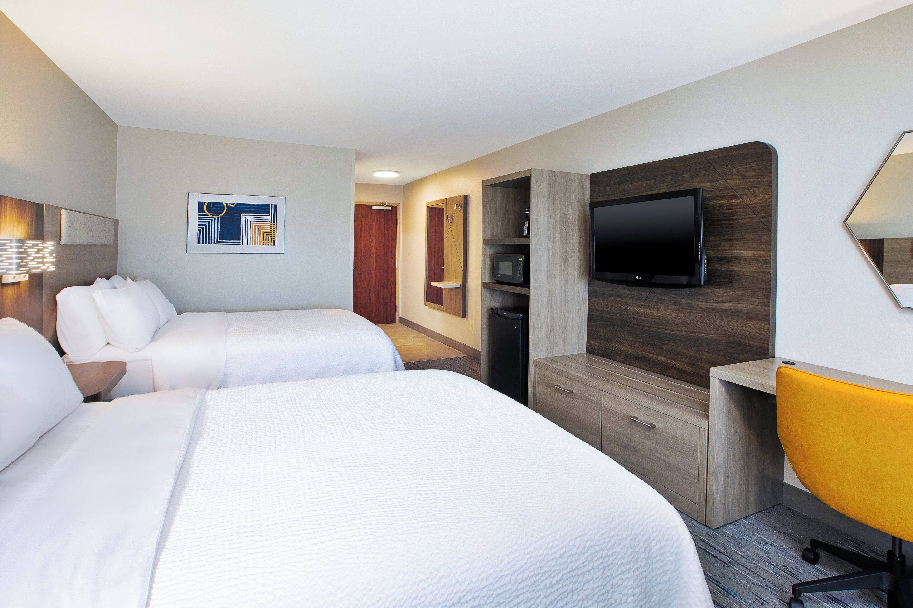 A hotel room with two beds, a TV, a microwave, and a desk with a chair.