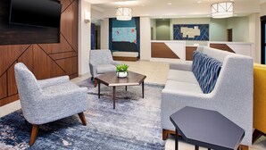 Eine moderne Hotelhalle mit einem großen Flachbildfernseher an der Wand, einer Sitzecke mit Sofas und Sesseln, einem Couchtisch mit einer Pflanze und einer Wandmalerei mit einer Karte.