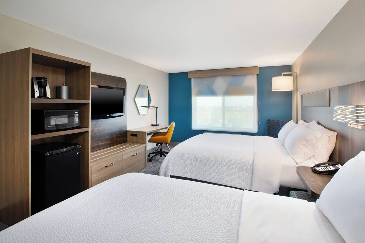 A hotel room with two beds, a desk, a chair, a TV, and a coffee maker.