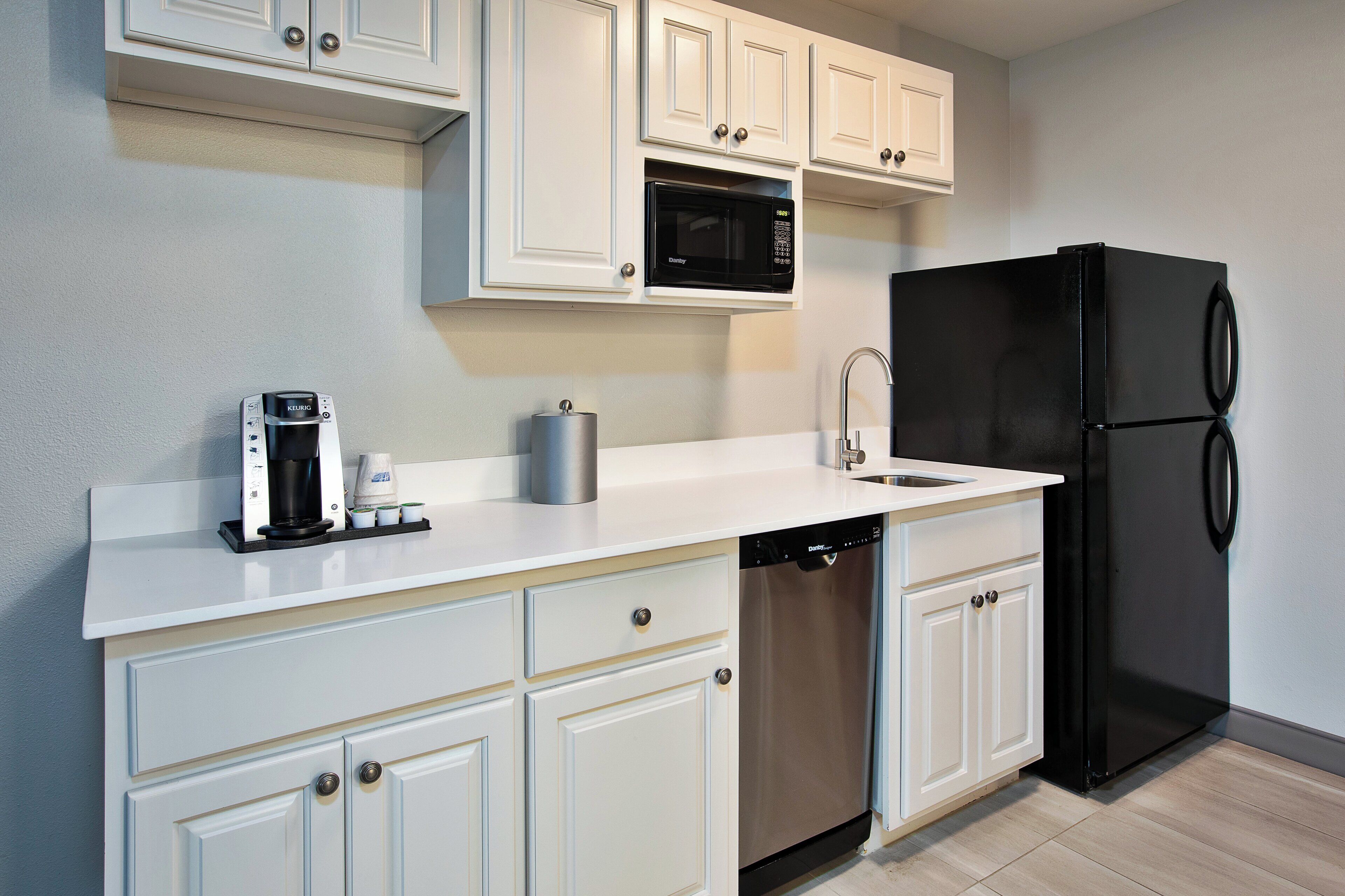 A kitchen with white cabinetry, a black refrigerator, a dishwasher, a coffee maker, and a microwave.