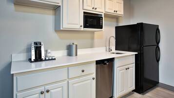 A kitchen with white cabinetry, a black refrigerator, a dishwasher, a coffee maker, and a microwave.