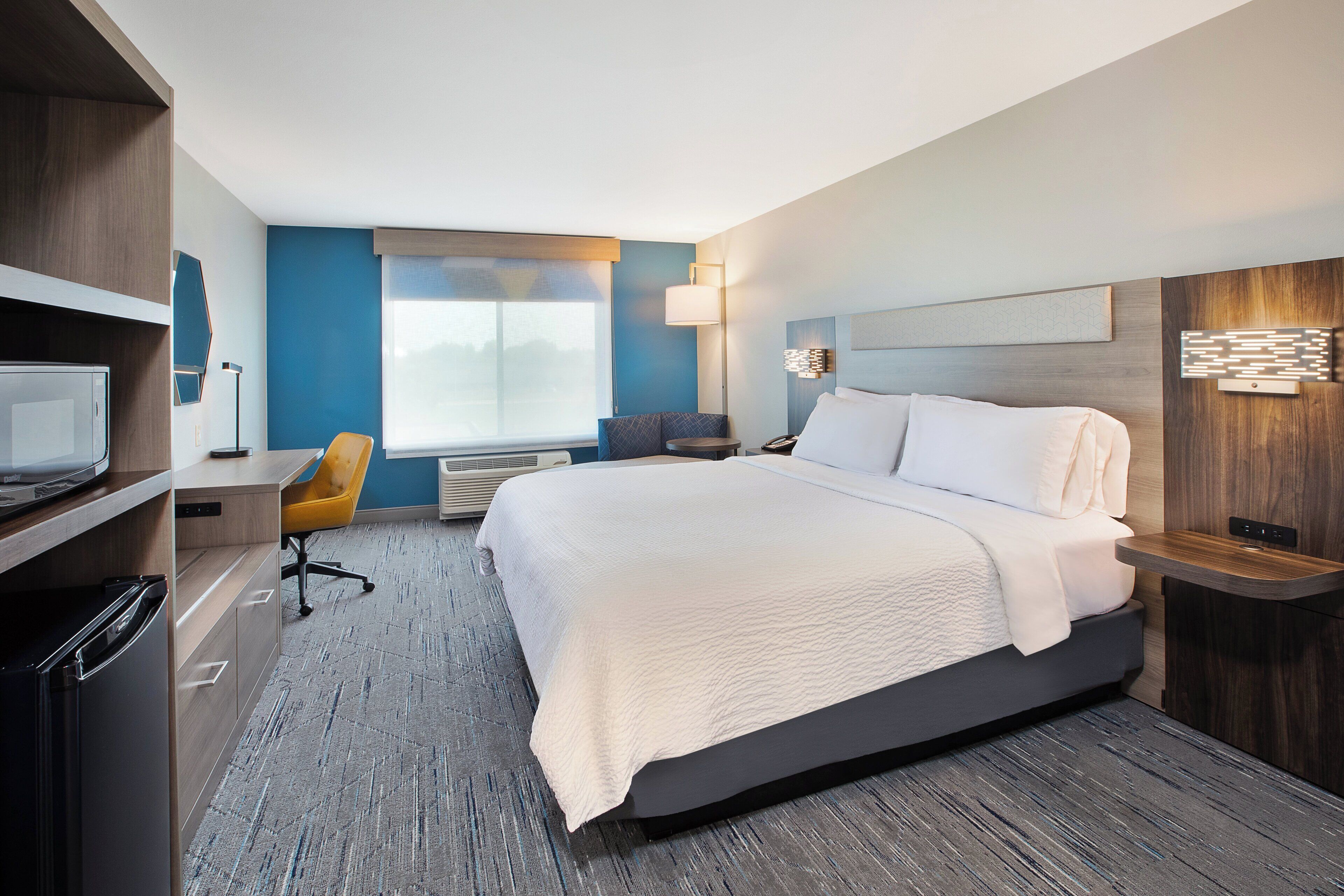 A modern hotel room with a large bed, a desk with a chair, a flat-screen TV, and a window with a view.