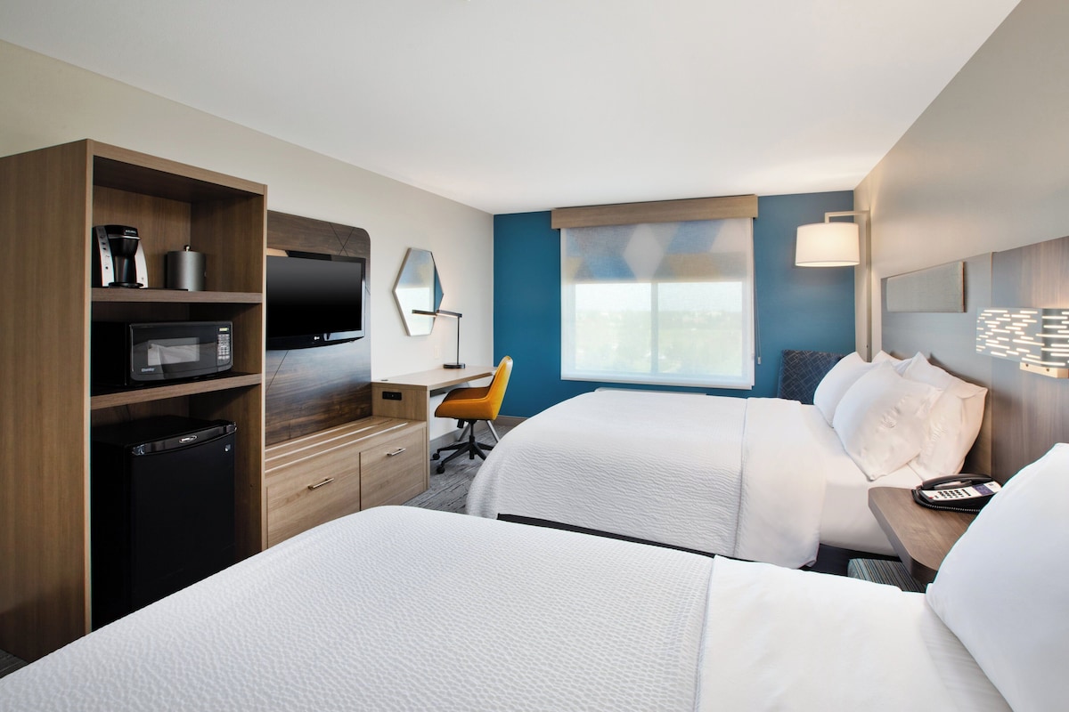 A hotel room with two beds, a desk, a chair, a TV, and a coffee maker.