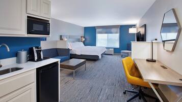 Habitación de hotel con cama, escritorio, silla, microondas, cafetera y lavamanos.