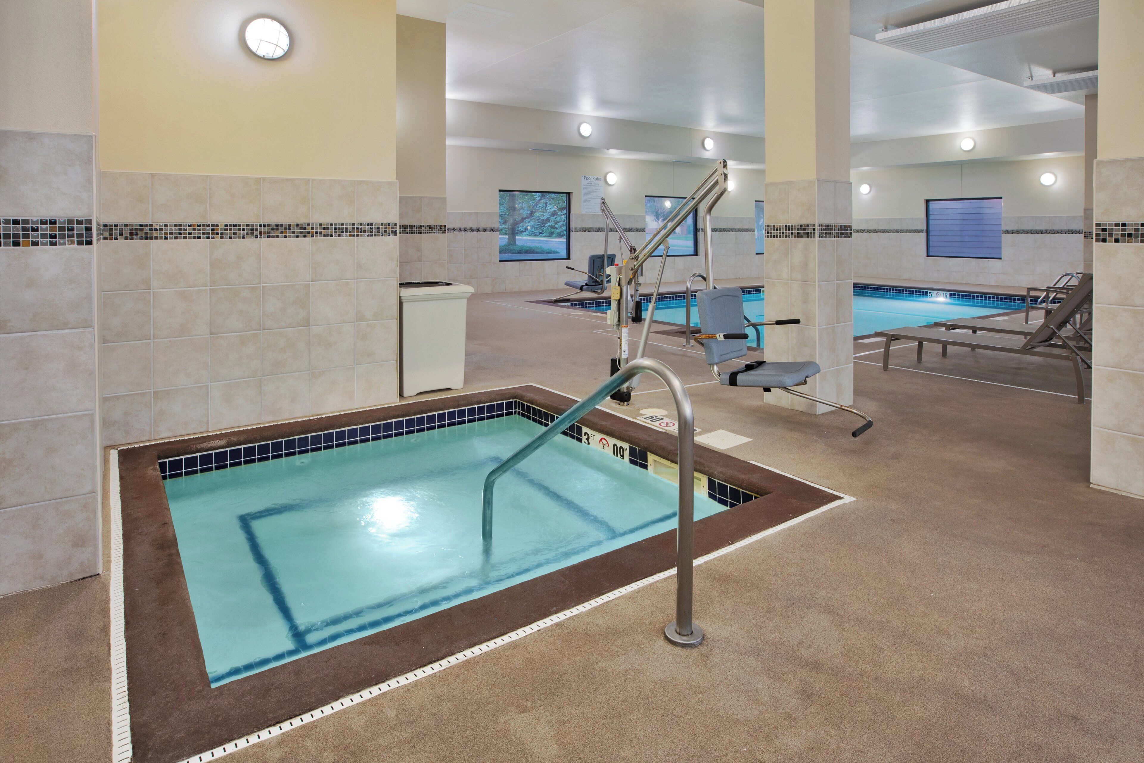 En swimmingpool med flisekant, omklædningsrum og et loungeområde med stole.