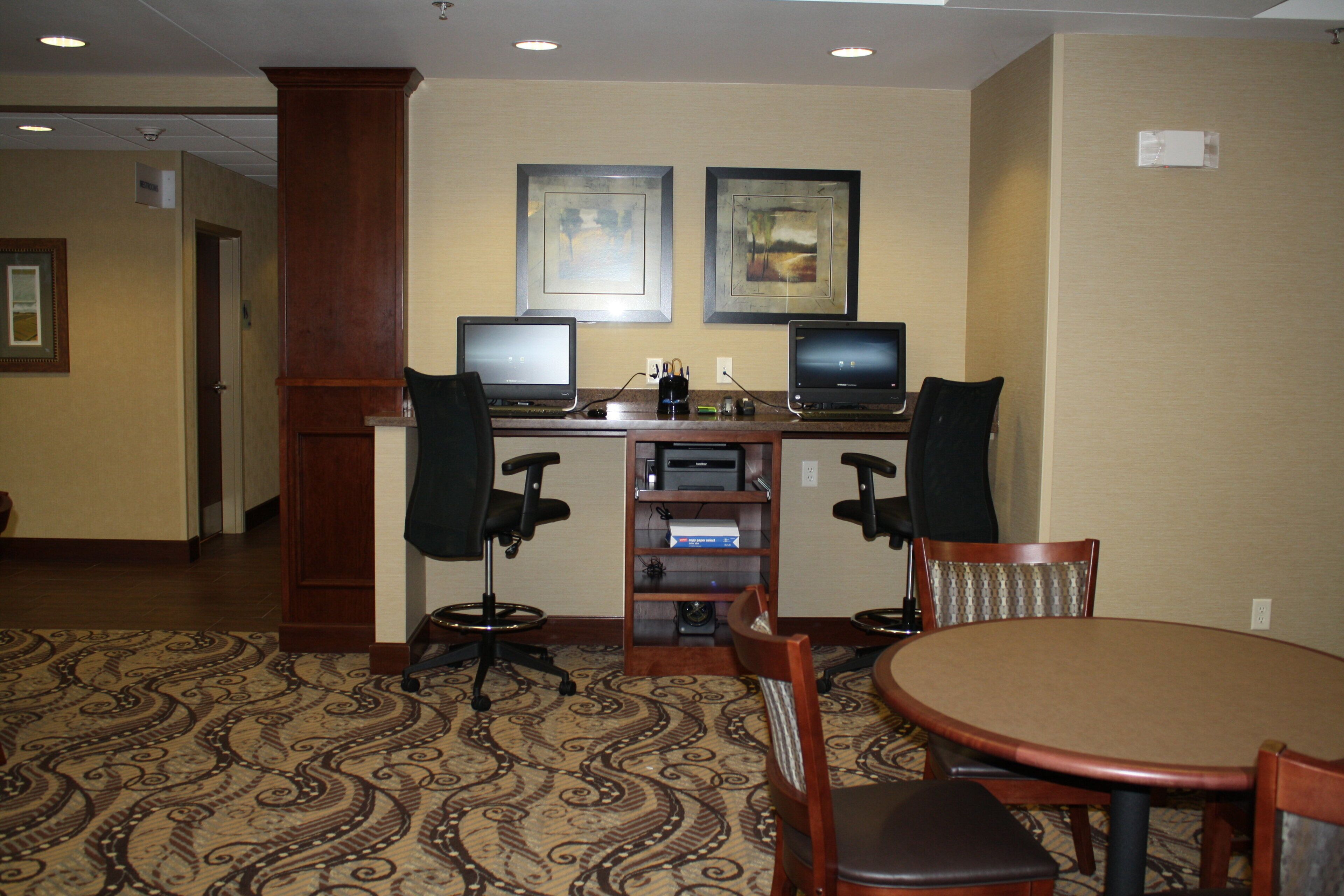 A hotel room with a desk, two monitors, a printer, and a conference table with chairs.