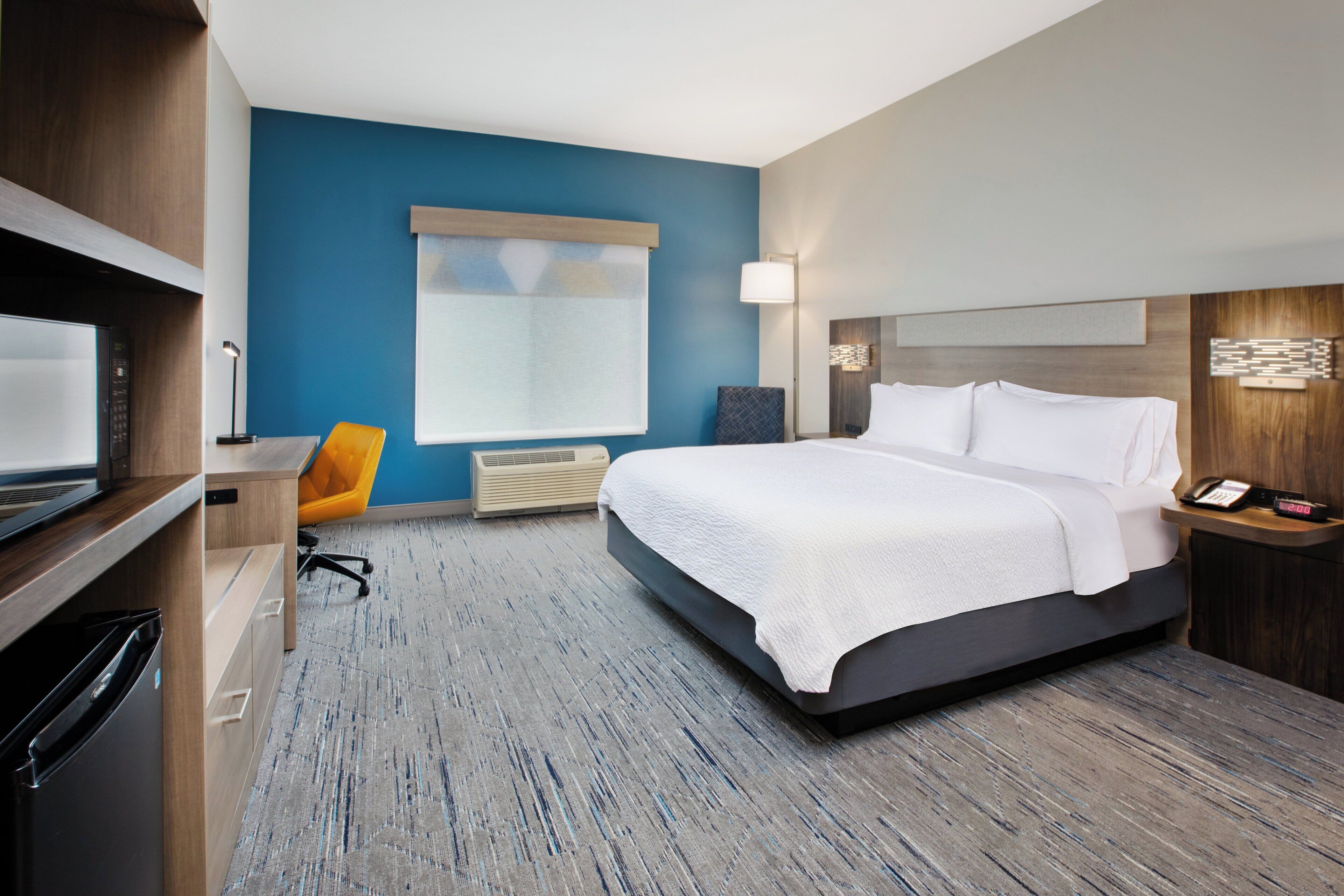 A hotel room with a bed, a desk, a chair, a TV, and a window with blinds.