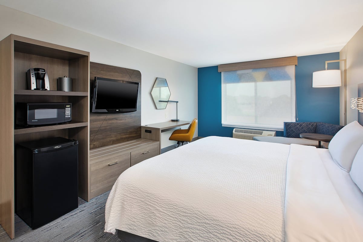 A hotel room with a bed, a desk, a TV, a coffee maker, and a mini-fridge.