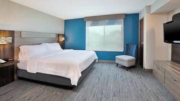 A modern hotel room with a large bed, a television, a small seating area, and a window with a view.