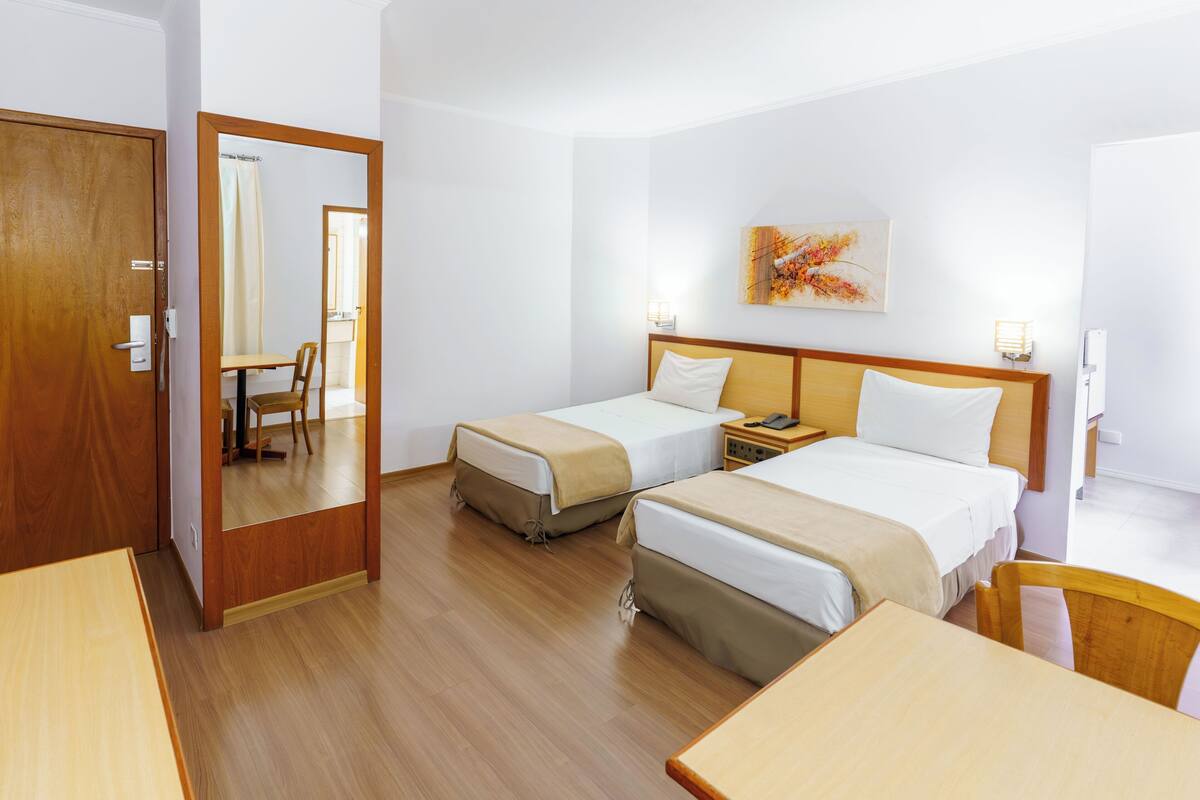 A hotel room with two beds, a wooden table, a chair, a nightstand, and a painting on the wall.