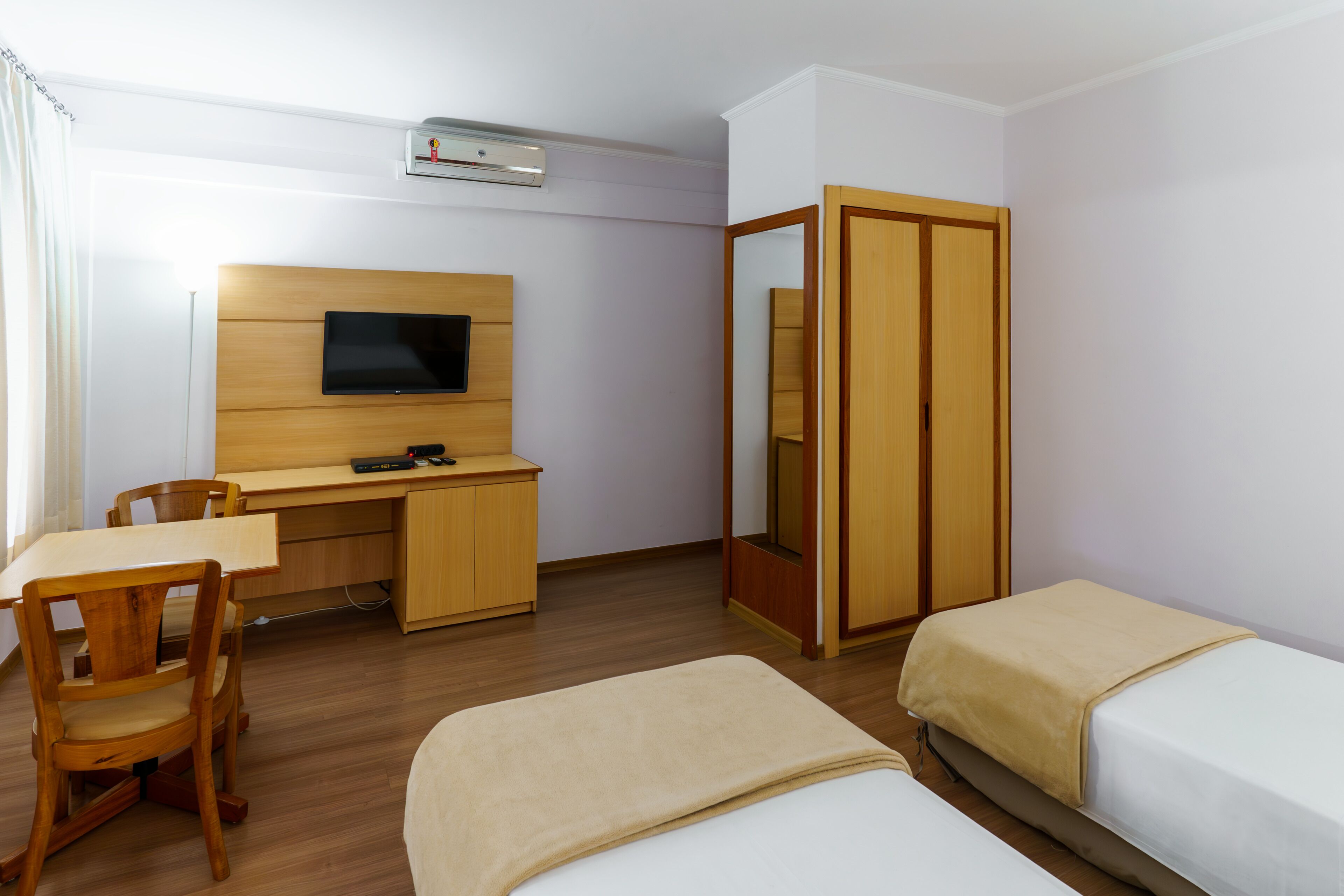 A hotel room with a wooden desk, a television, a wardrobe, and two beds.