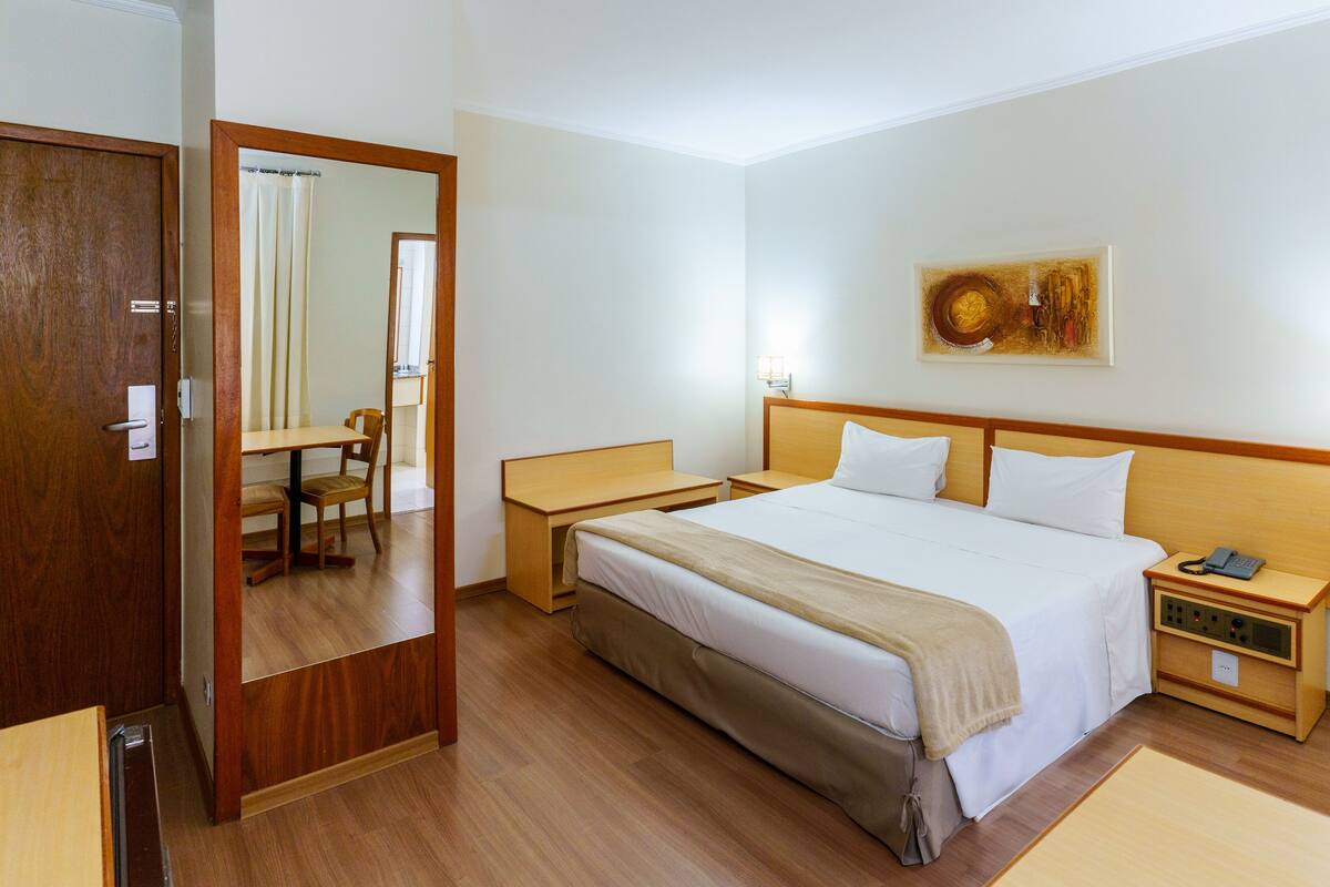 A hotel room with a wooden bed, bedside tables, a chair, a desk, and a mirror.