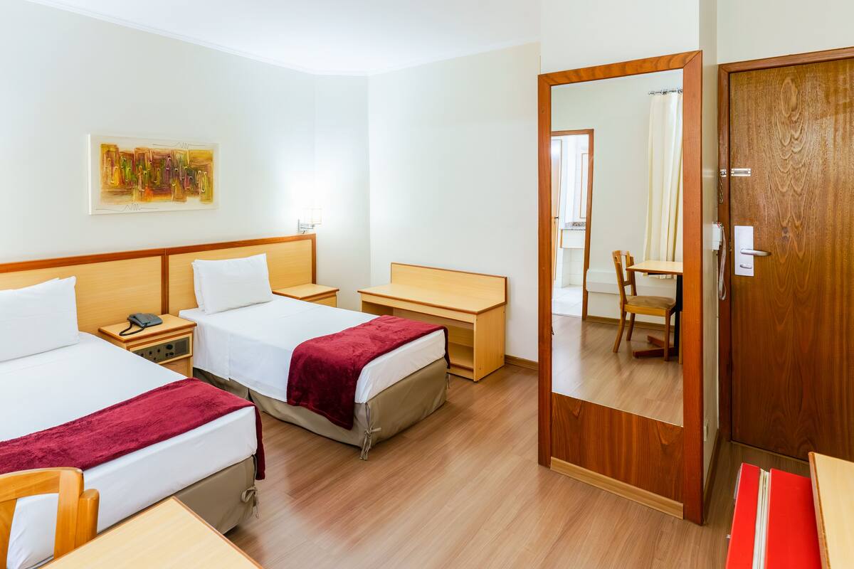 A hotel room with two beds, a desk, a chair, and a wardrobe.