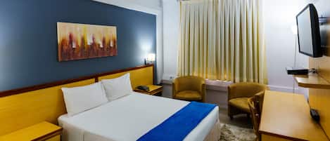 A hotel room with a bed, bedside tables, a desk, a chair, a television, a painting on the wall, and a window with curtains.
