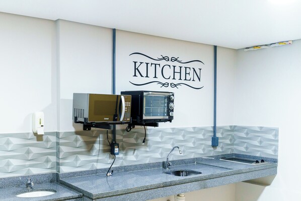Una cocina con mostrador, pileta y horno microondas instalado en la pared.
