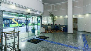 A modern lobby with a glass entrance, a reception desk, a potted plant, and a blue tactile path. - Hotel Augusta Boulevard (São Paulo)