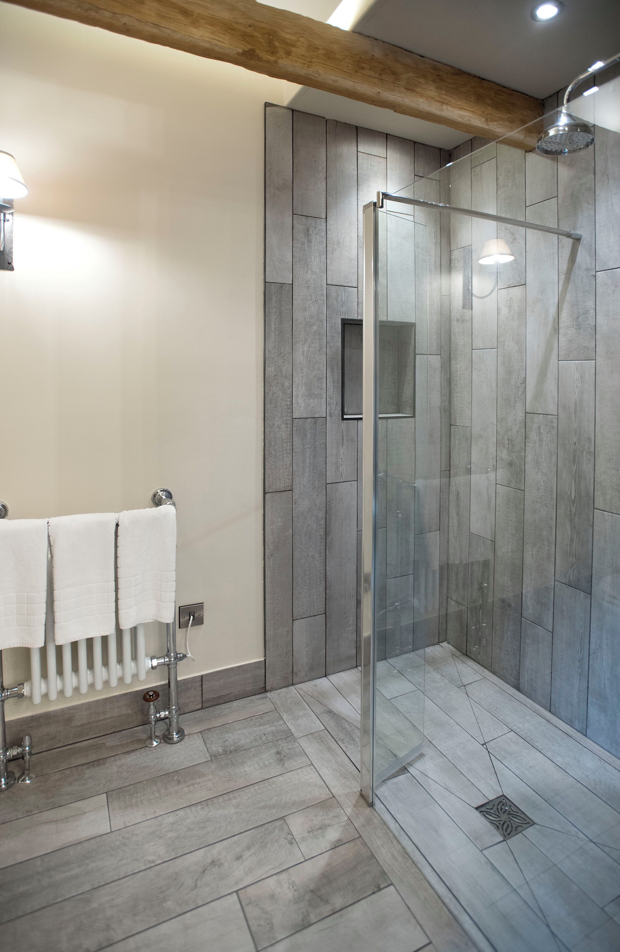 Un baño moderno con una ducha envuelta en vidrio, un toallero blanco y un radiador.
