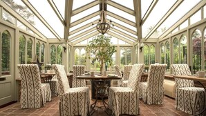 A conservatory with a high ceiling, patterned chairs, a central table, and a chandelier. - Holly Lodge Boutique B&B (Fakenham)