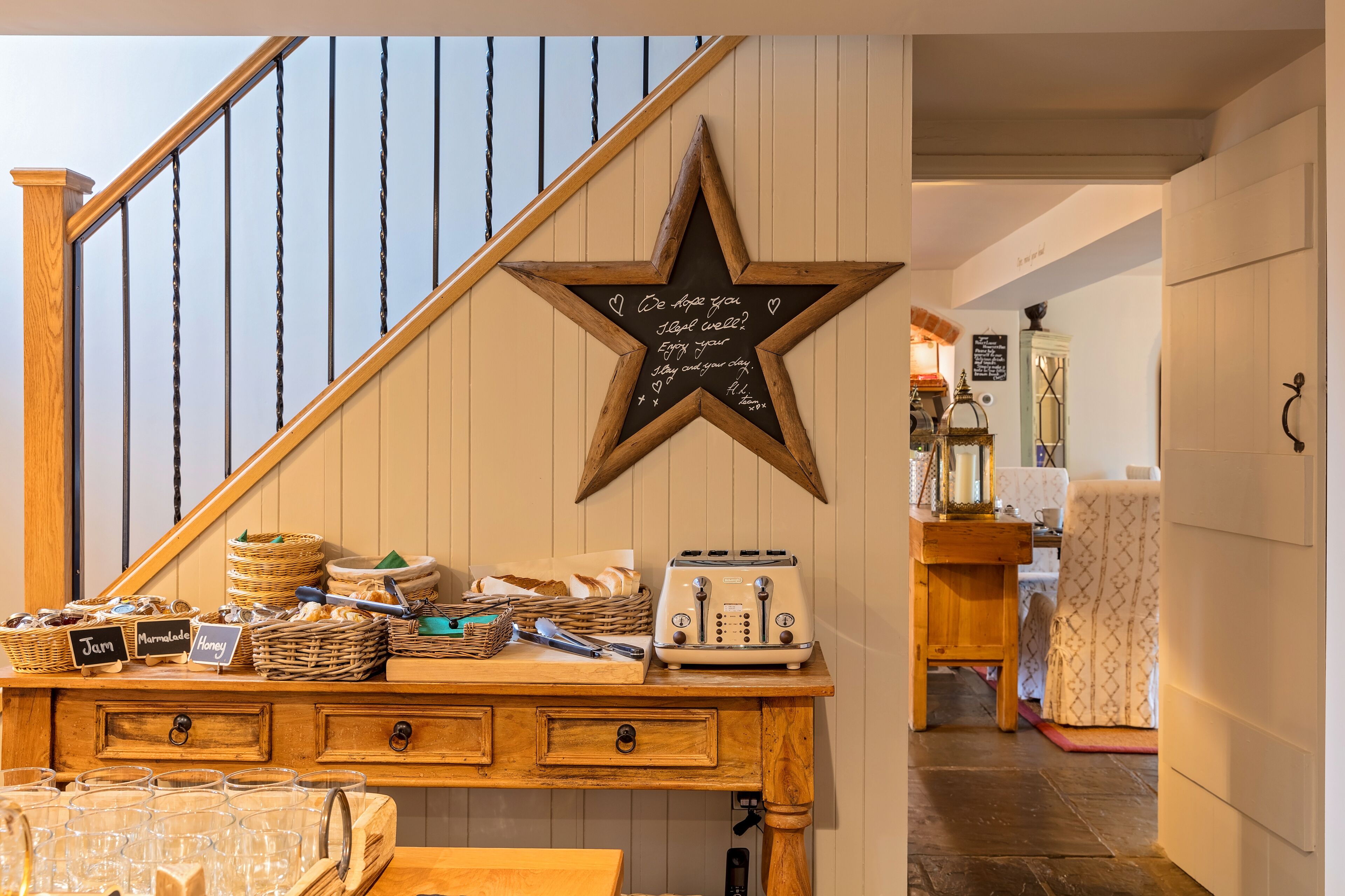 A wooden counter with baskets labeled "Jelly," "Marmalade," and "Honey," a vintage toaster, and a star-shaped sign with a message.
