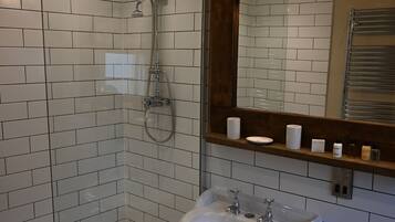 A bathroom with a glass-enclosed shower, a pedestal sink, and a mirror with a wooden shelf above it.