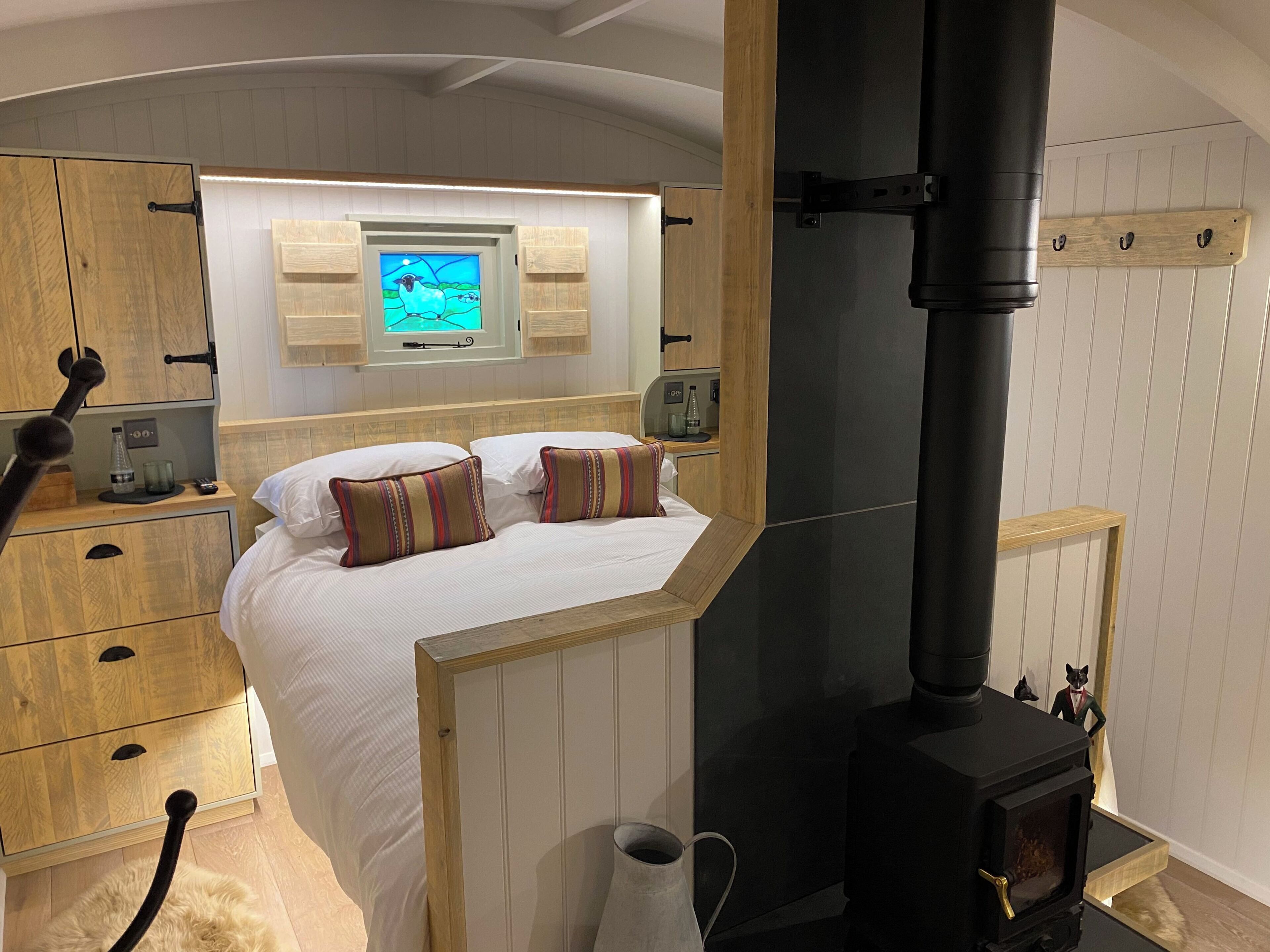Un dormitorio con cama, armario de madera, televisor montado en la pared, estufa negra y una pequeña estatua.