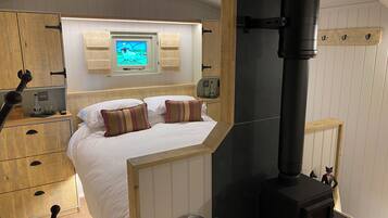 Un dormitorio con cama, armario de madera, televisor montado en la pared, estufa negra y una pequeña estatua.