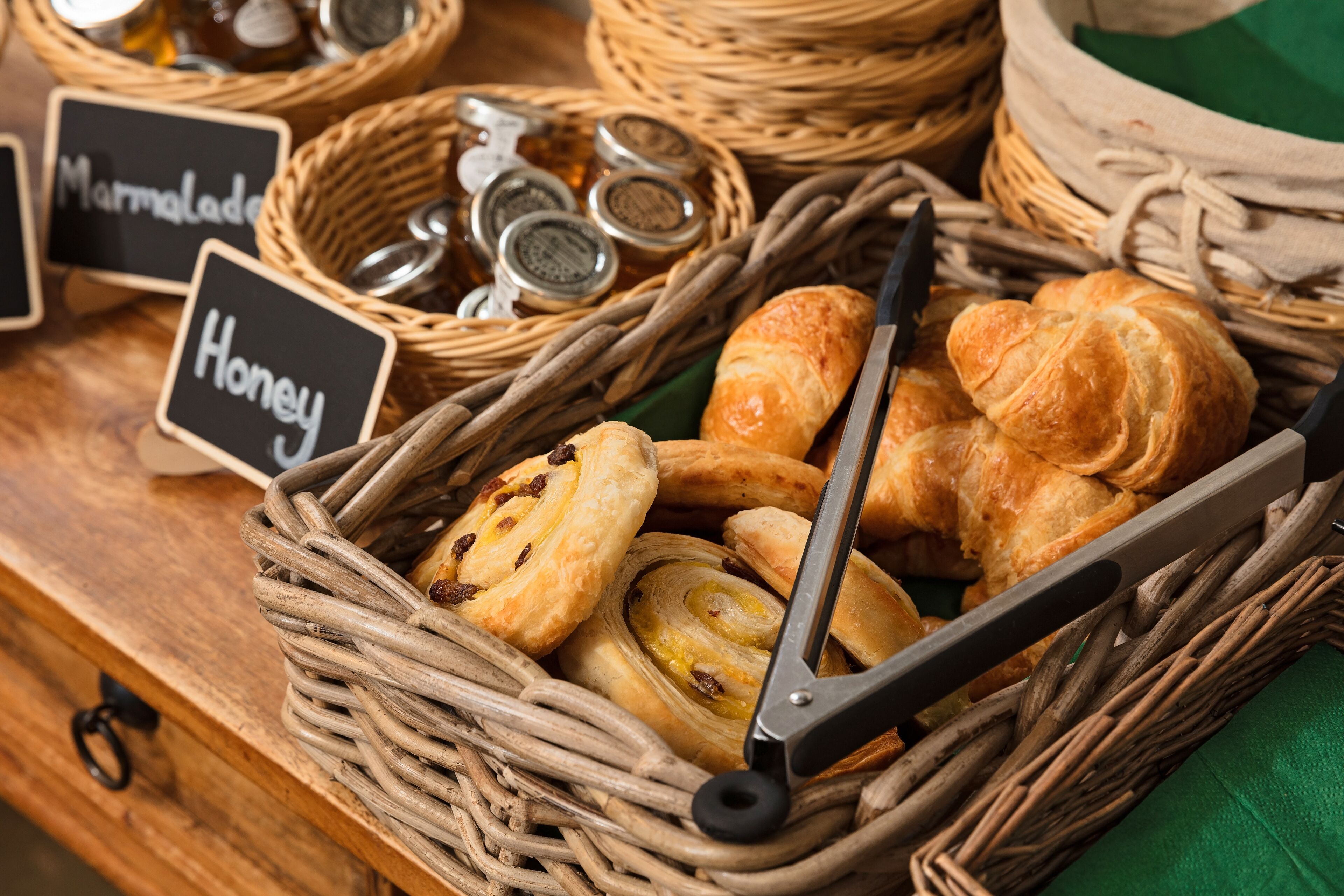 A wicker basket filled with pastries and honey jars, with labels indicating 'Marmalade' and 'Honey'.