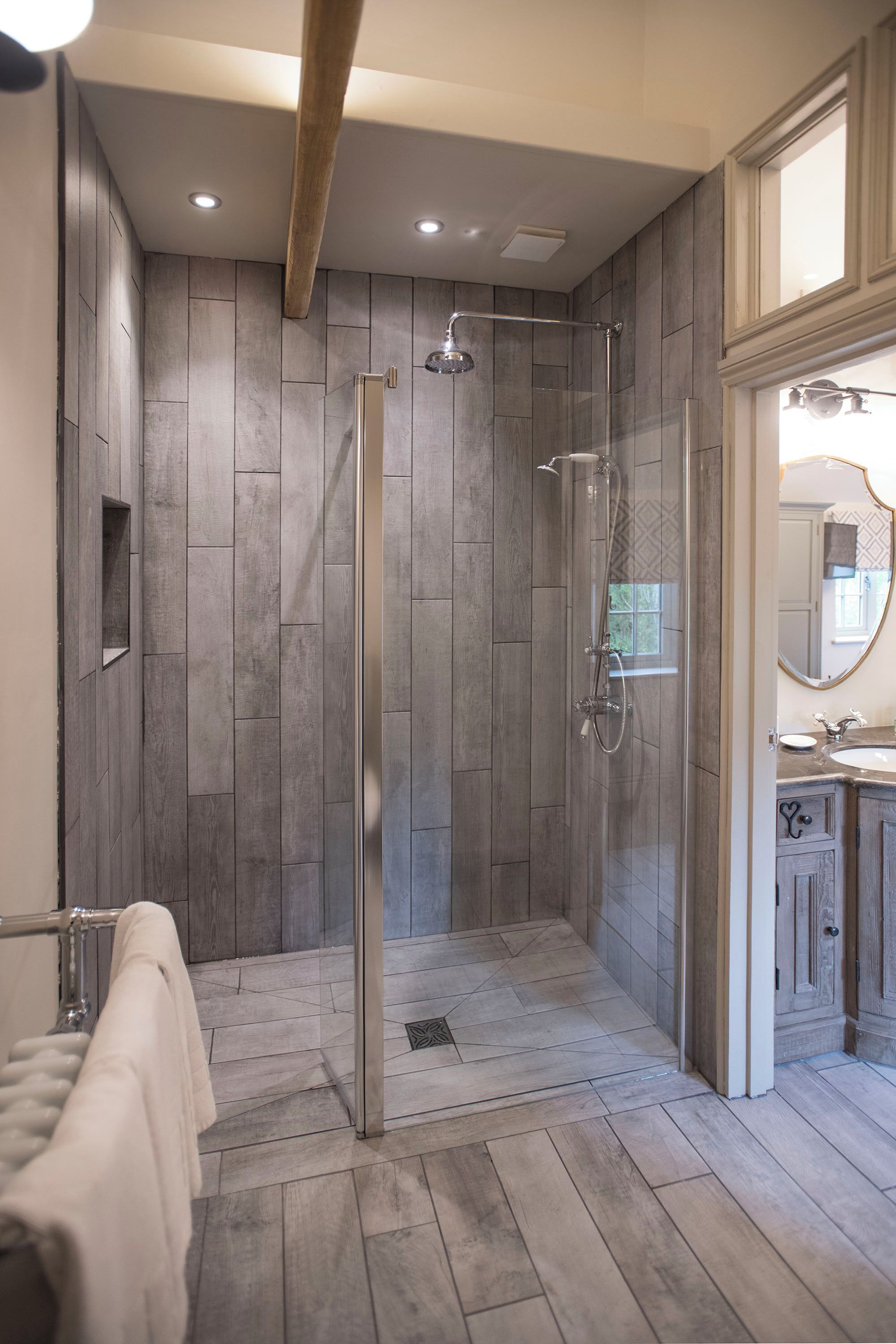 A modern bathroom with a glass-enclosed shower, wooden flooring, and a vanity with a mirror.