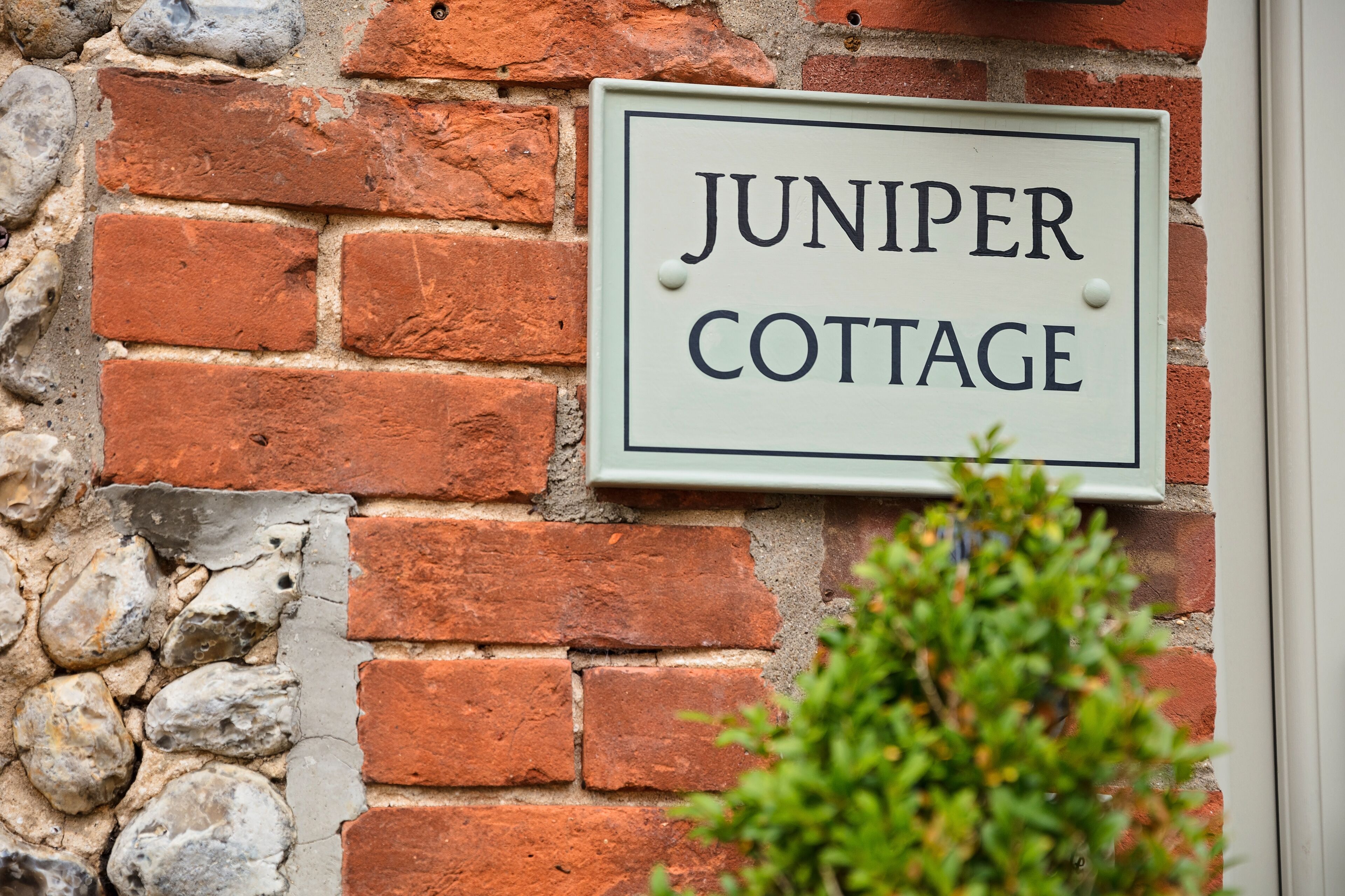A sign reading "JUNIPER COTTAGE" mounted on a brick wall.