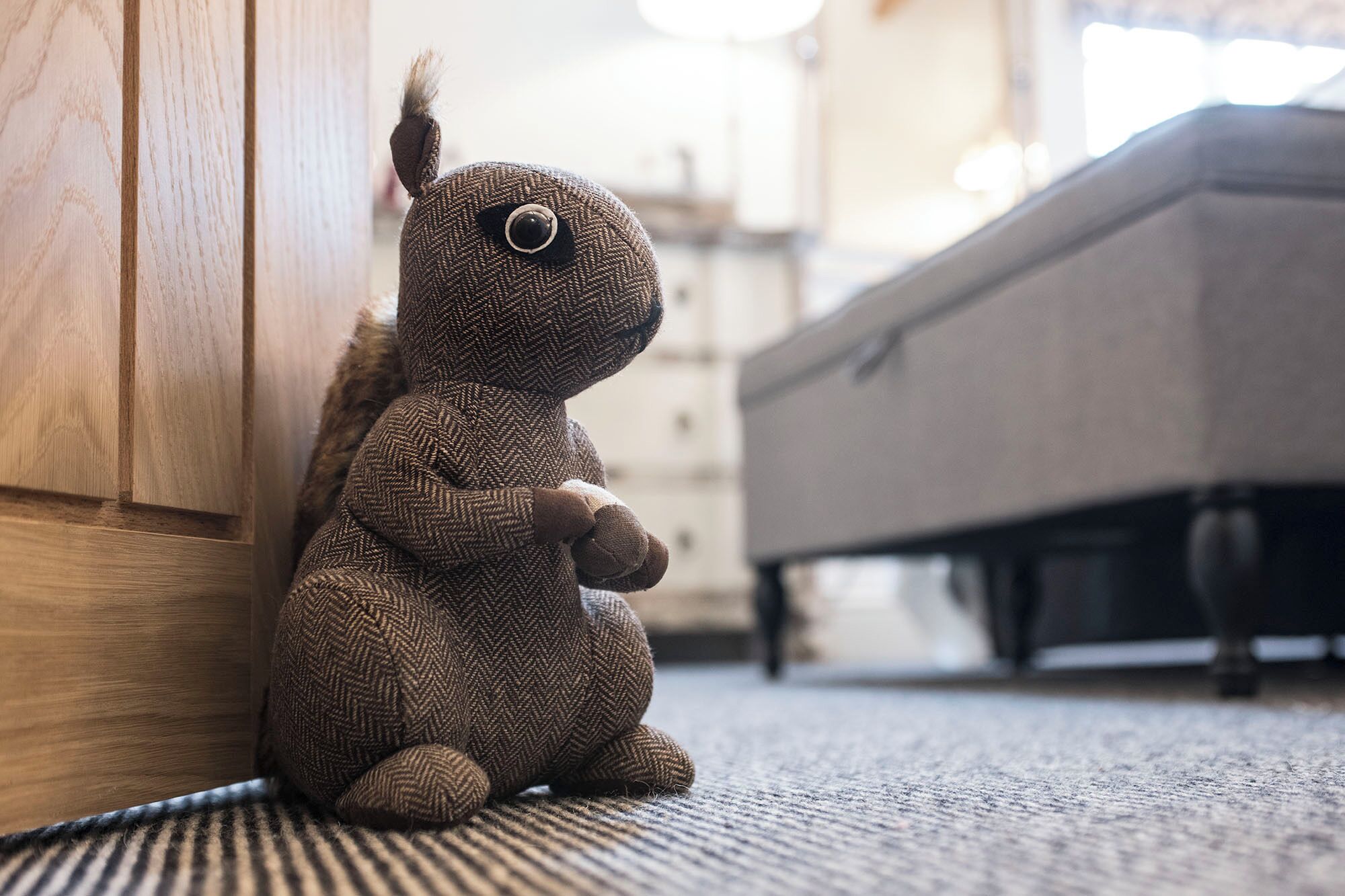 A plush toy sitting on a carpeted floor next to a wooden door and a bed.