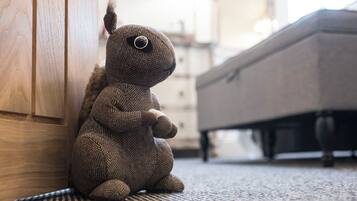 A plush toy sitting on a carpeted floor next to a wooden door and a bed.