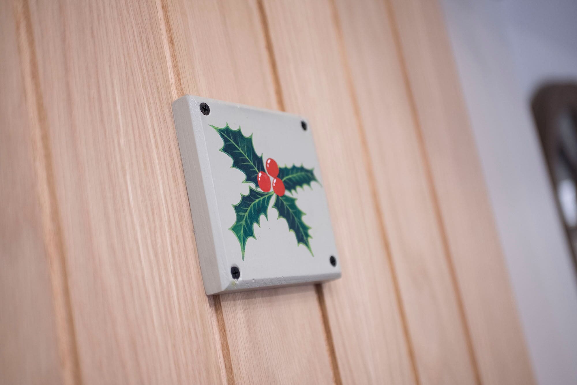 A small, square, white plaque with a holly design on a wooden surface.