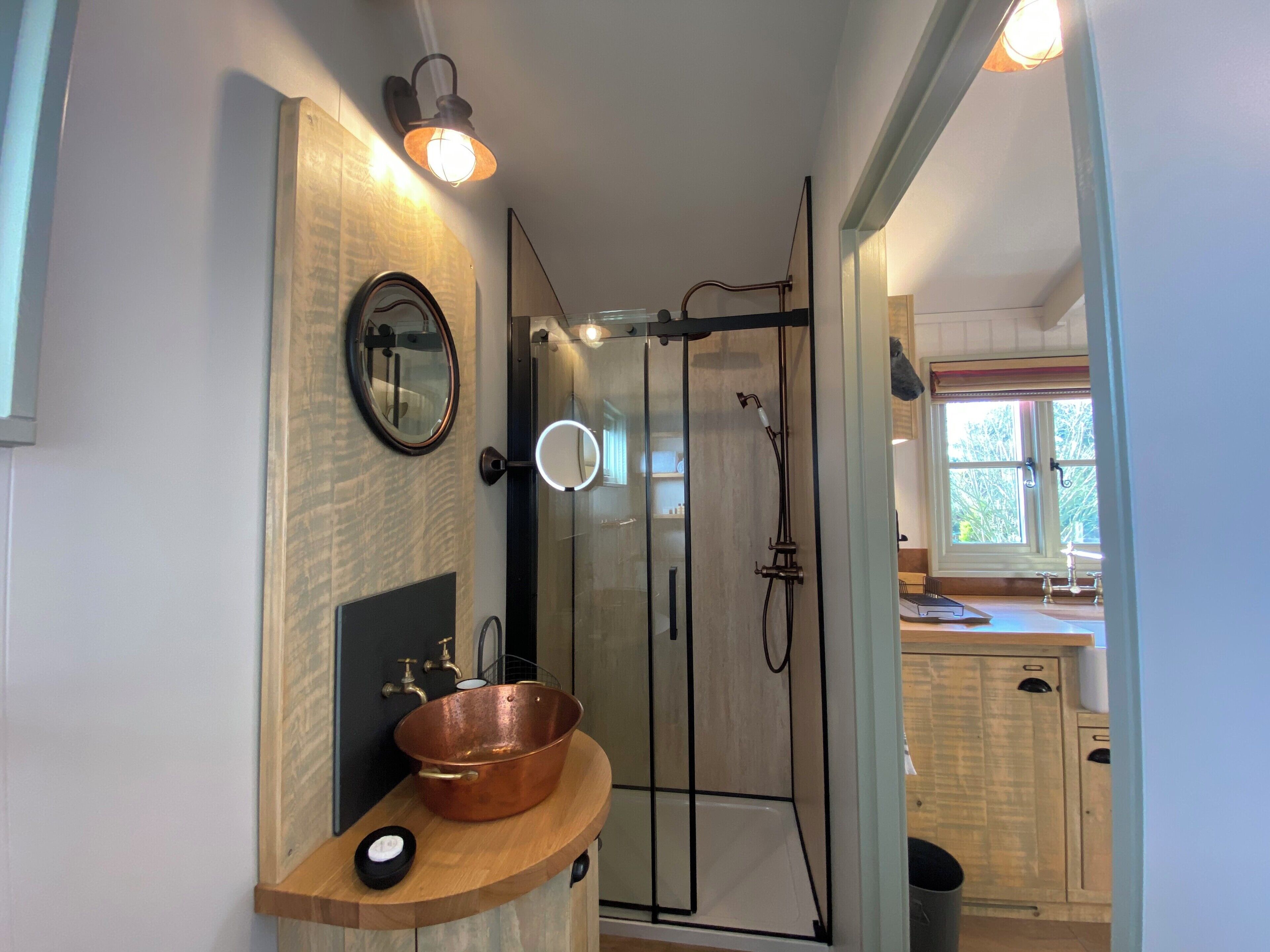 Un baño moderno con ducha de vidrio, un lavabo de cobre sobre encimera de madera y un espejo sobre el lavamanos.