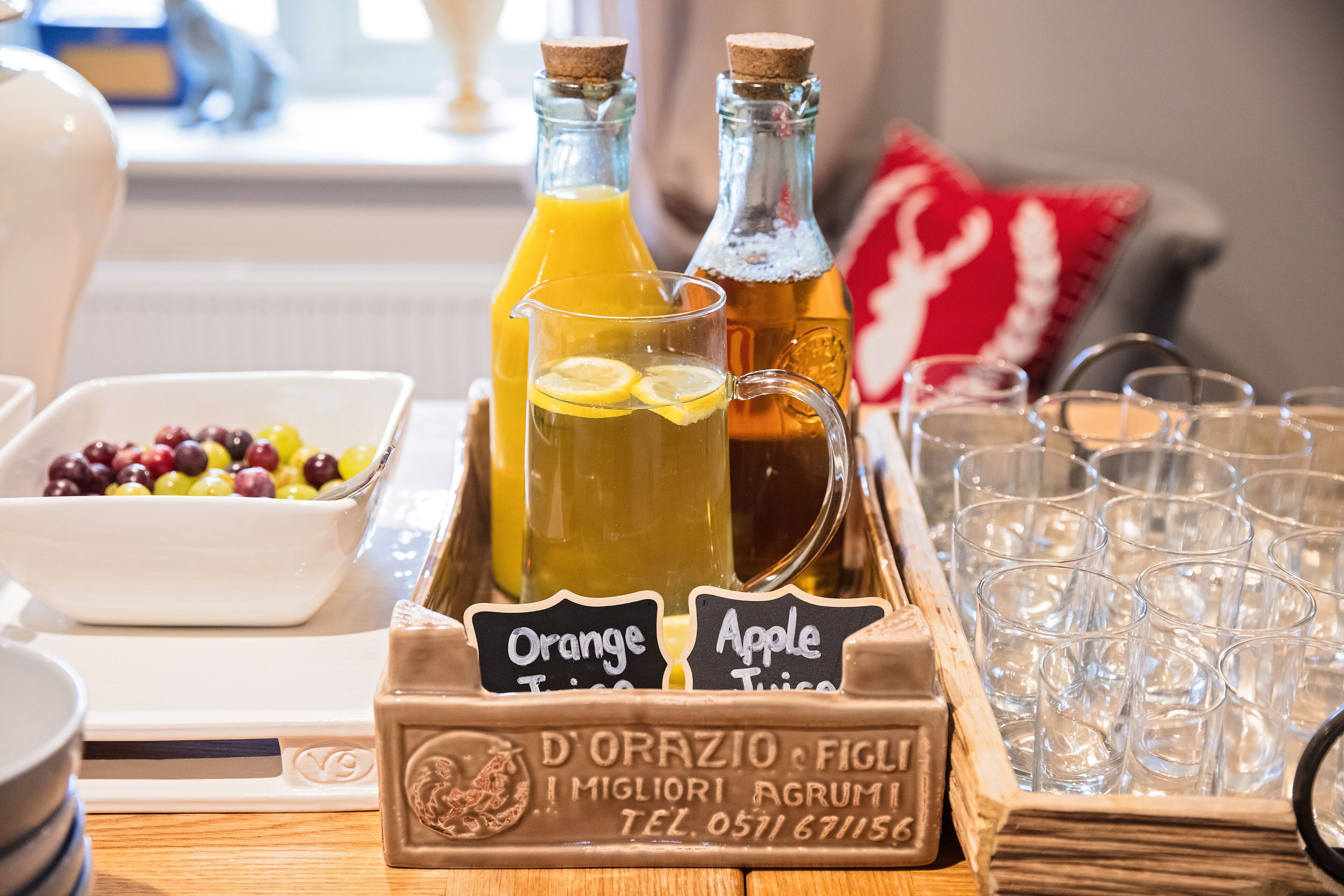 A breakfast setup with orange and apple juice bottles, a bowl of mixed berries, and a tray of glasses.