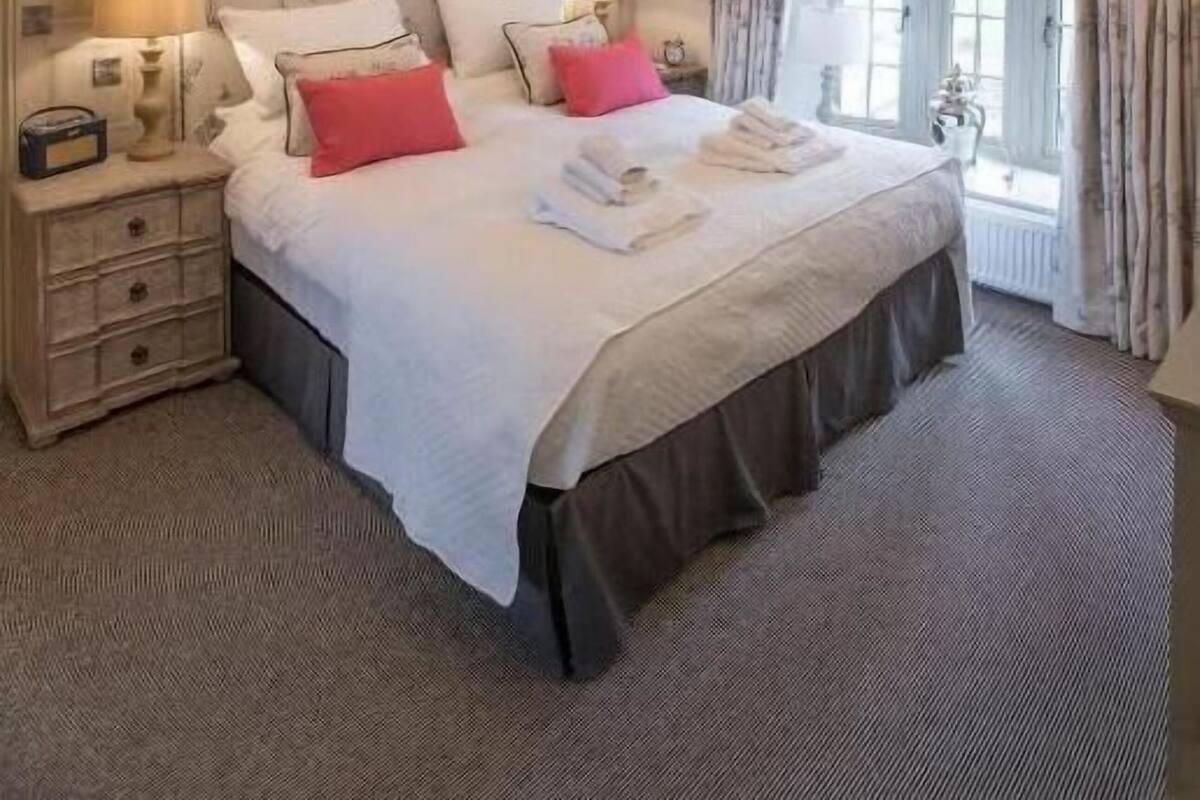 Un dormitorio espacioso con una cama grande, una araña, un reloj y una ventana con cortinas.