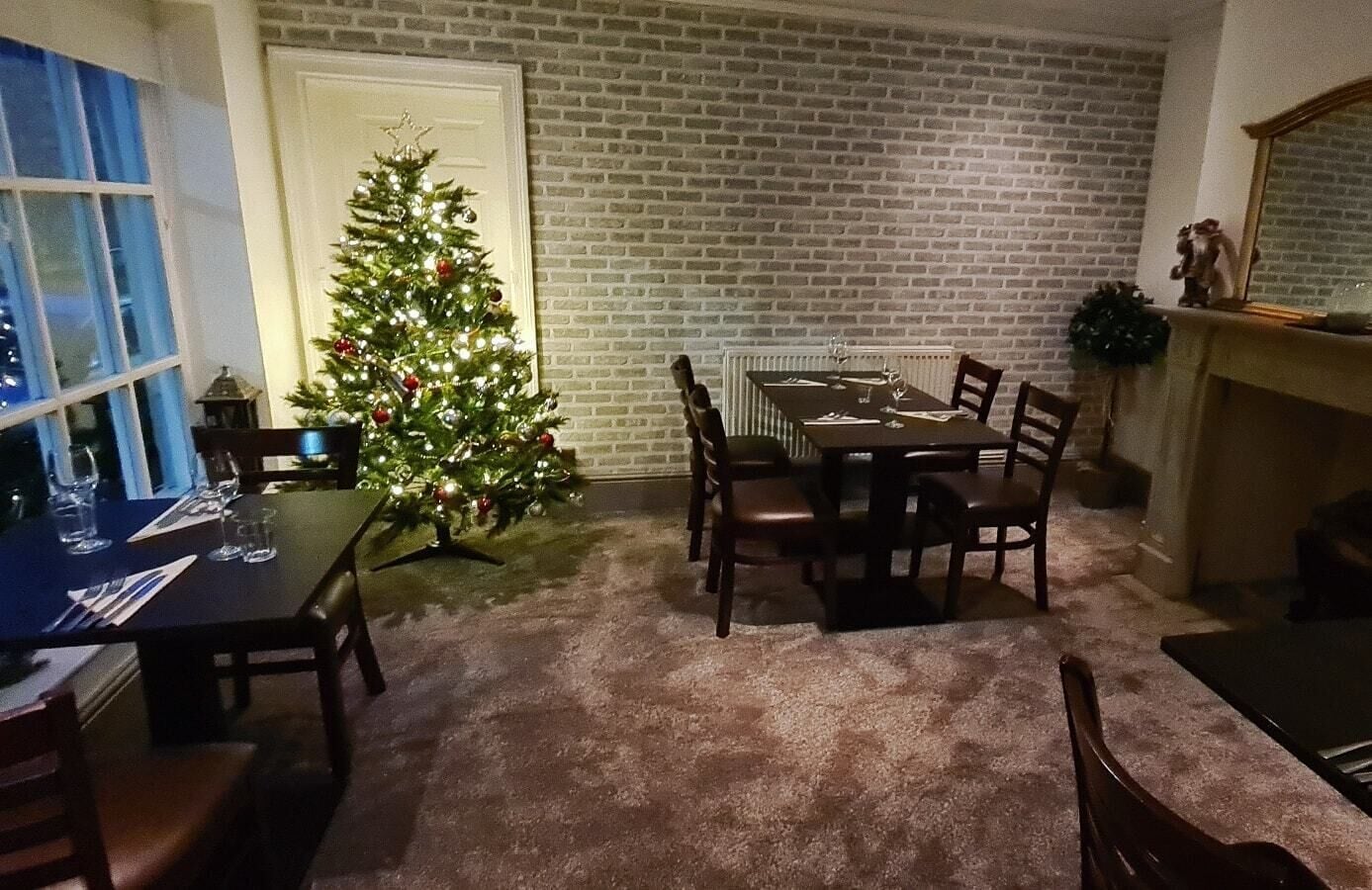 A dining area with a brick wall, a Christmas tree, and a fireplace.