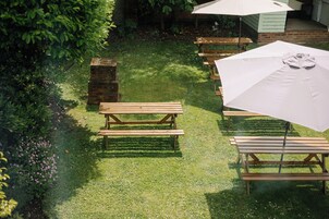 Un espacio al aire libre con césped, mesas de picnic de madera y un paraguas grande.