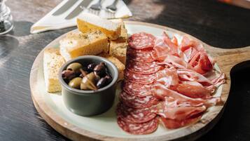 Una tabla de madera con salami en rodajas, un bol de aceitunas y trozos de pan sobre una mesa.
