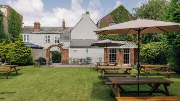 A courtyard with picnic tables and umbrellas, surrounded by brick buildings and greenery.