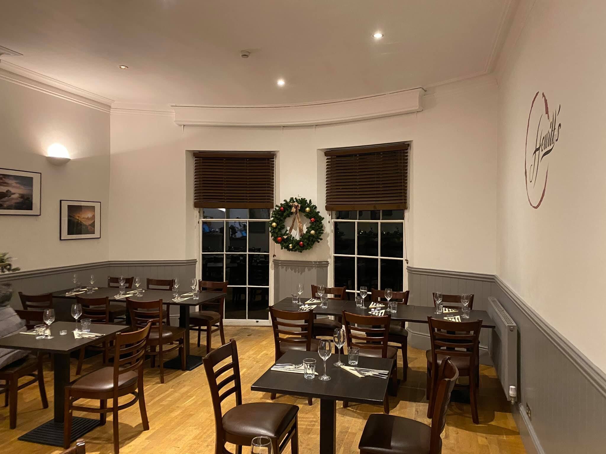A dining area with multiple tables and chairs, a fireplace, and a Christmas wreath on the wall.