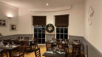 A dining area with multiple tables and chairs, a fireplace, and a Christmas wreath on the wall.
